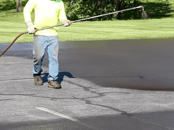 Worker spraying a fresh coat of sealer across an asphalt surface